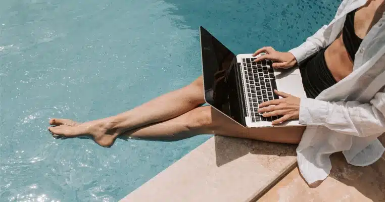 woman sitting on poolside using laptop