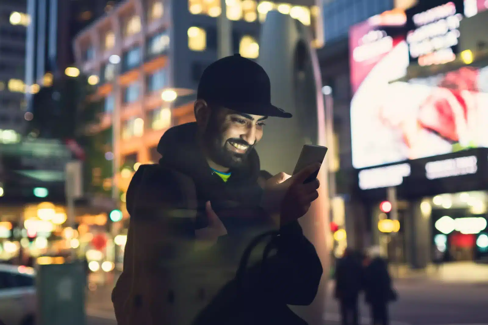 A smiling man holding a phone while standing on a street
