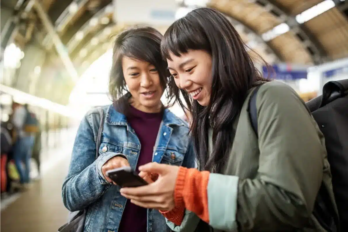 Dos mujeres sonriendo y usando un teléfono móvil.