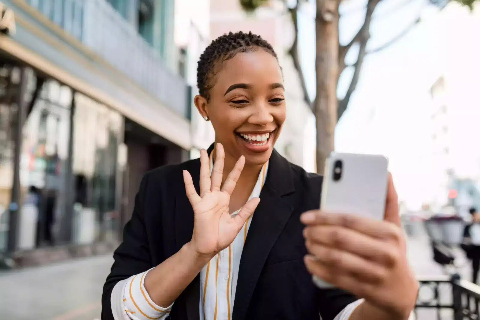 A woman happily waving and smiling at her phone while standing outdoors