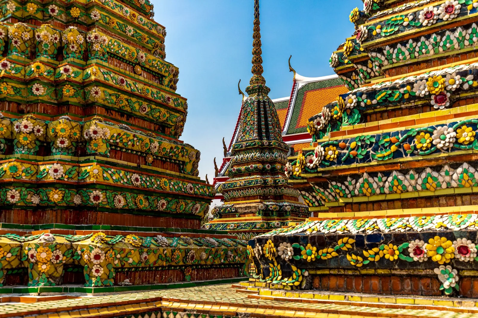 The colorful and ornate stupas of the Wat Pho temple in Bangkok, porcelain mosaics and golden spires under a clear blue sky