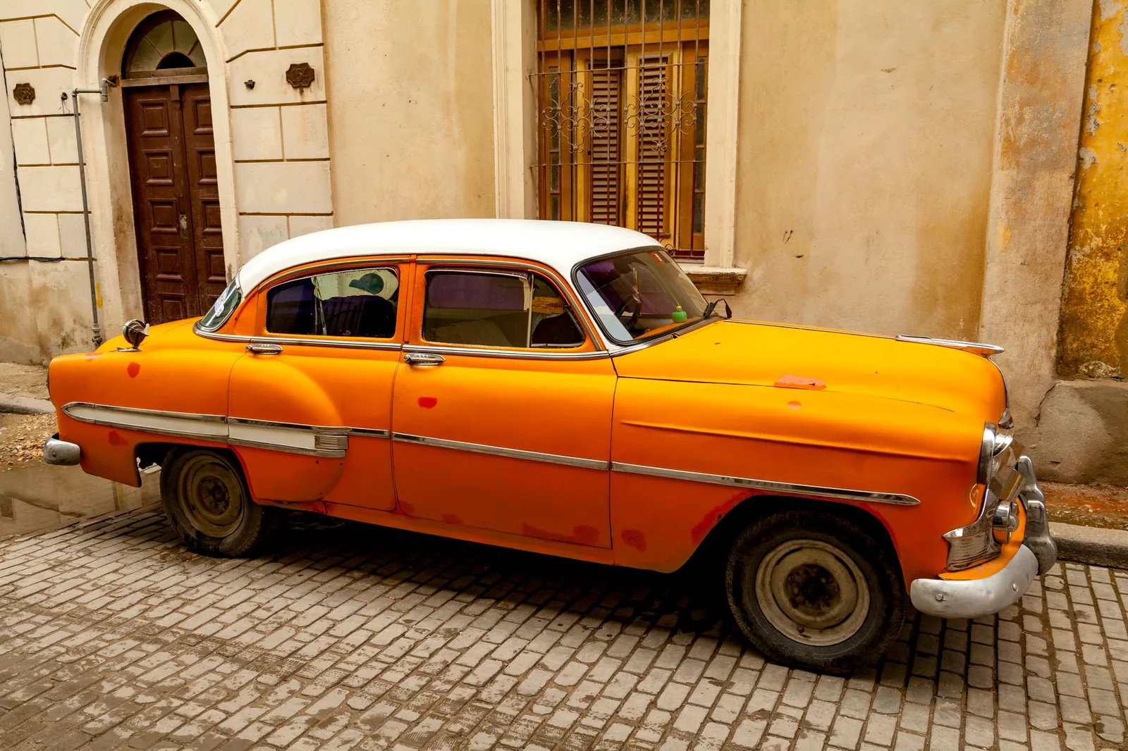 Coche americano vintage naranja aparcado en una calle empedrada de La Habana, Cuba