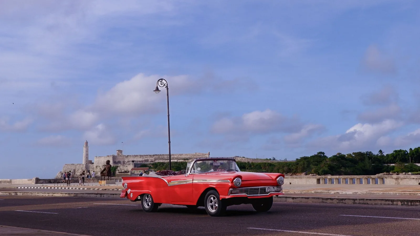 Descapotable rojo por el Malecón de La Habana con la fortaleza El Morro al fondo, Cuba