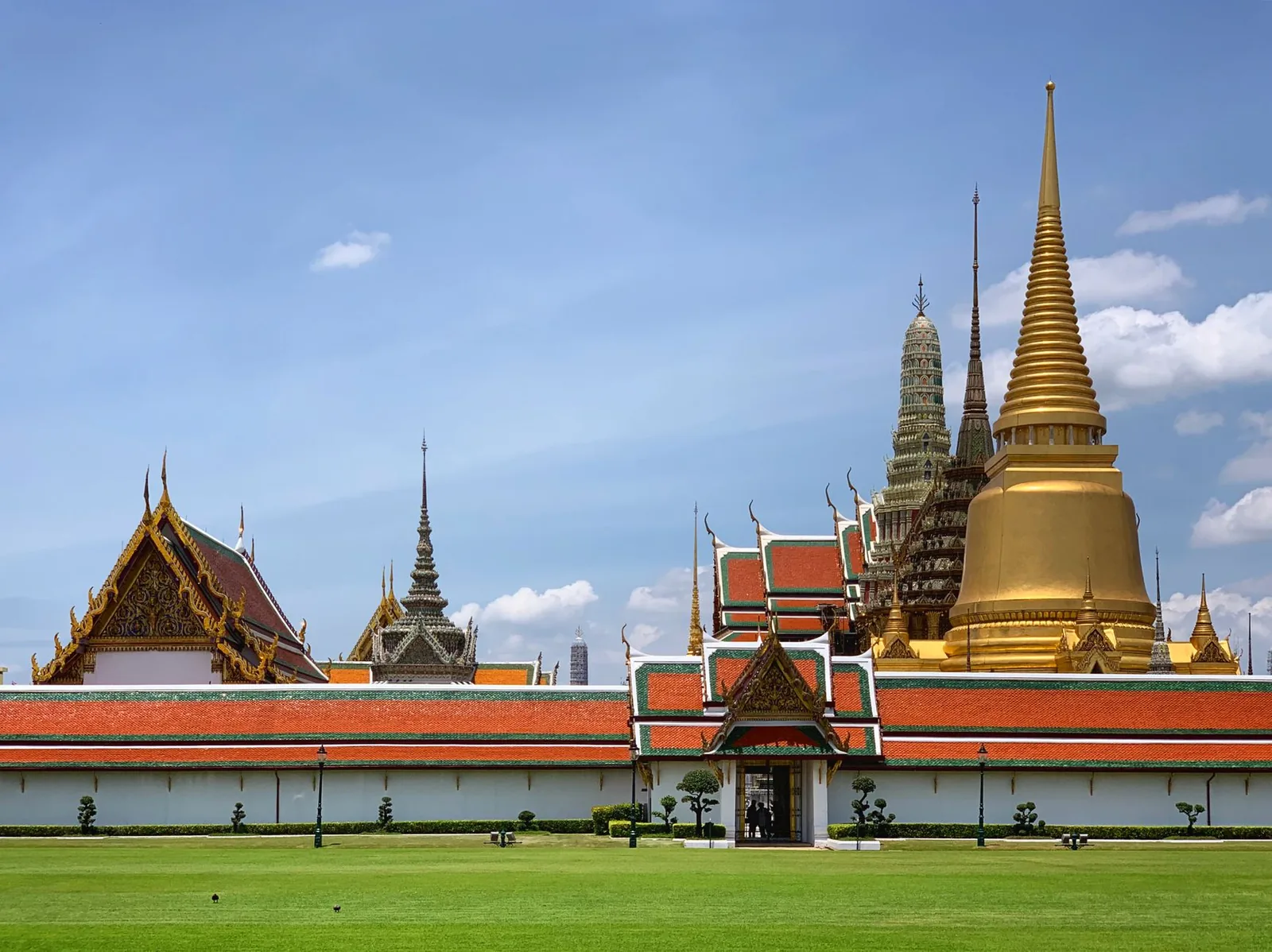 The Grand Palace in Bangkok with its golden spires gleaming in the sun, traditional Thai architecture under a blue sky
