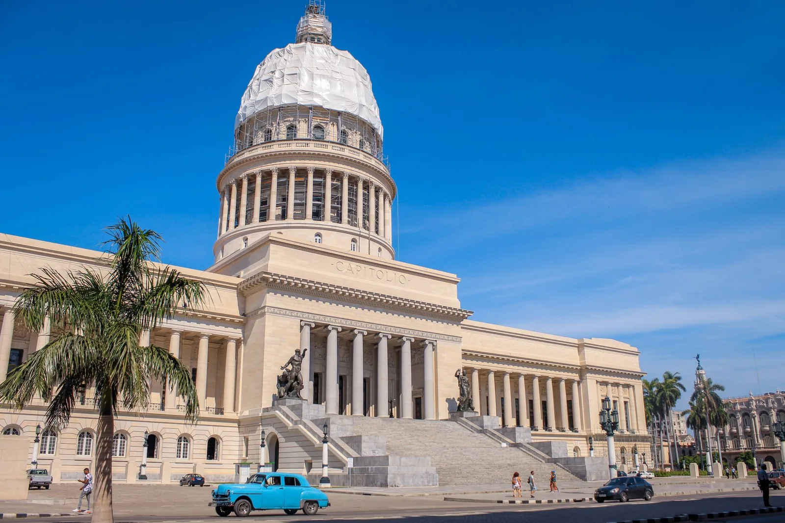 Havana's Capitol building under a blue sky, with a palm tree and a vintage American car, Cuba