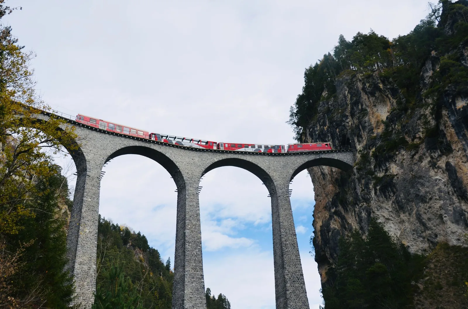 A red train crossing the stone arches of the Landwasser Viaduct in the Swiss Alps