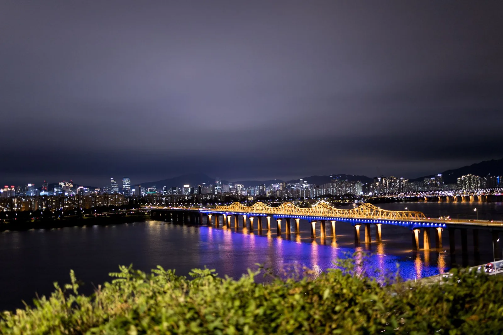 Puente iluminado sobre el río Han en Seúl de noche, con los rascacielos de la ciudad al fondo