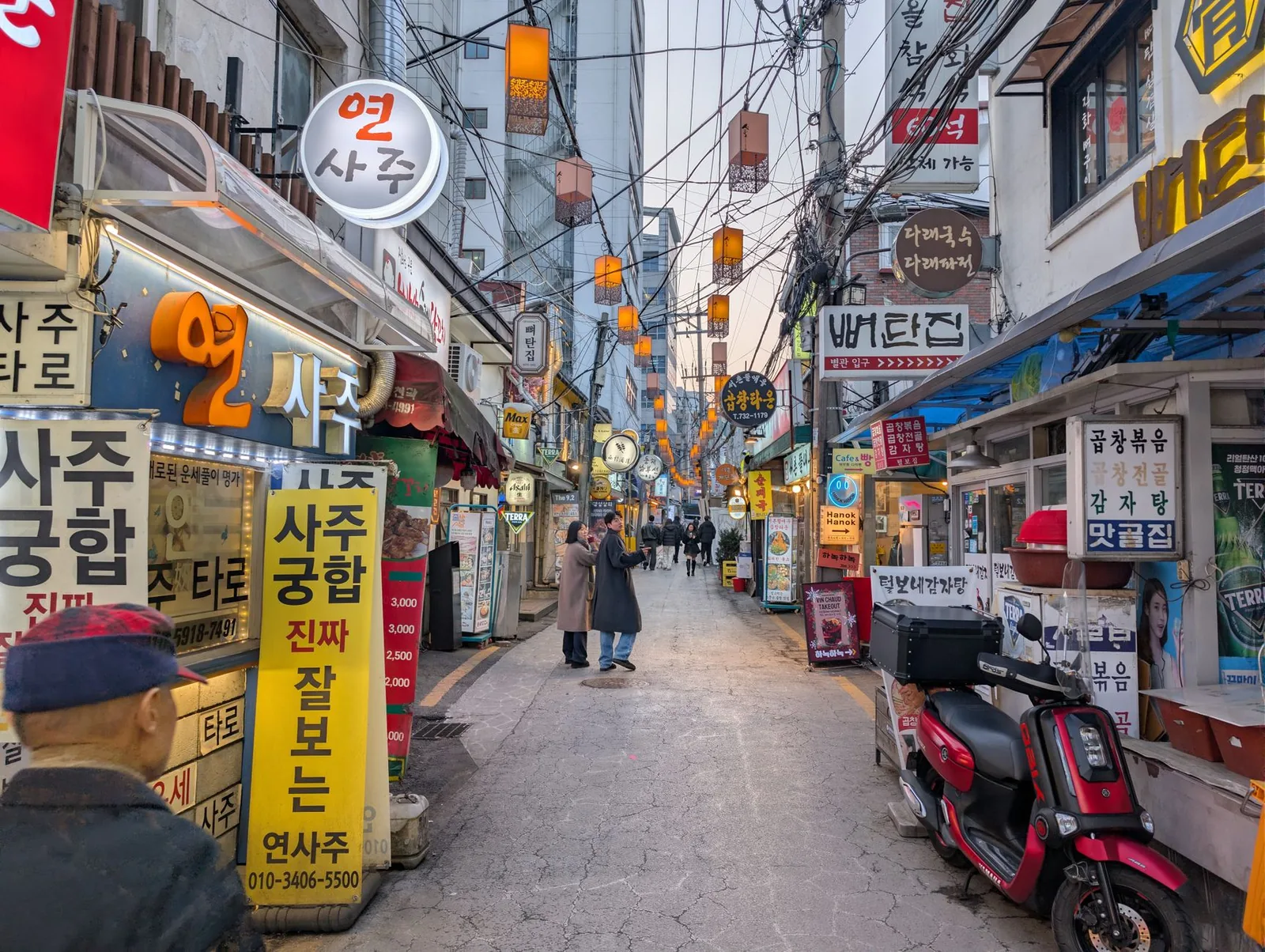 A lively Seoul alley in the evening, glowing signs and warm lighting along the small shops