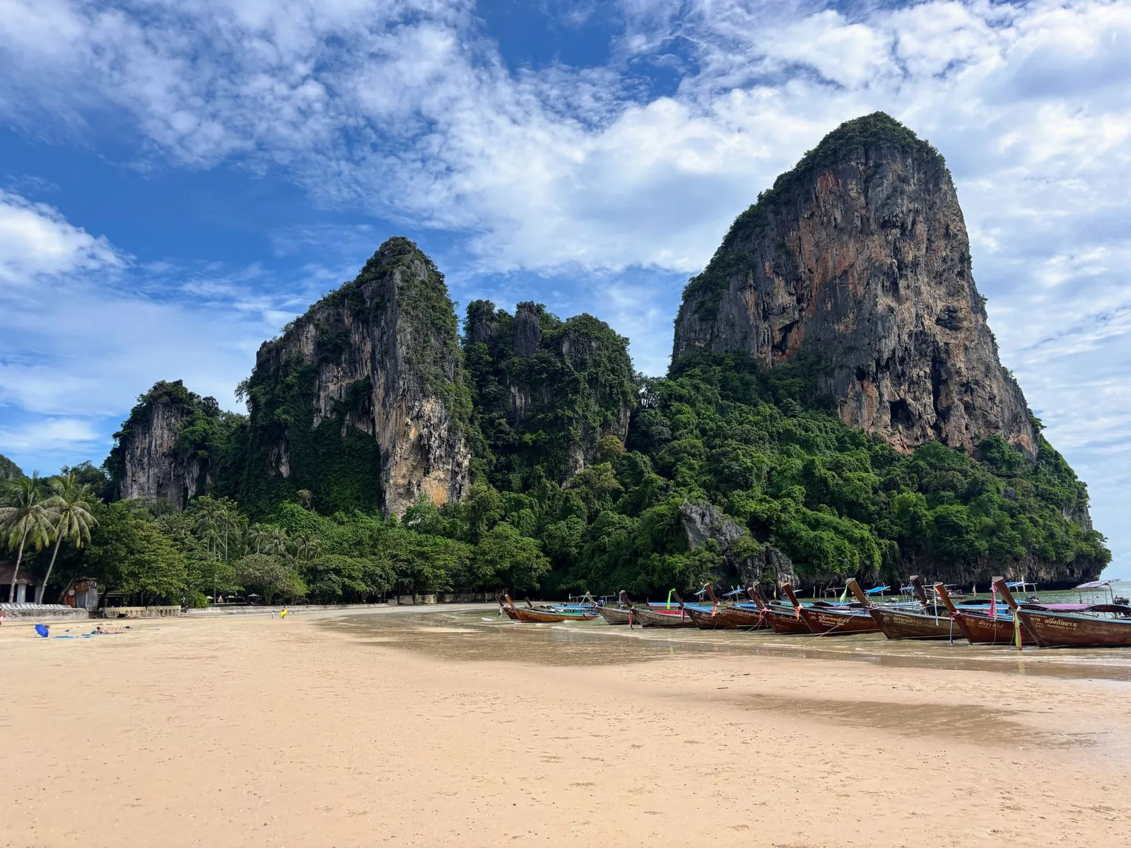 Railay Beach in Krabi, Thailand, with wooden long-tail boats lined up on the sand at the foot of dramatic limestone cliffs