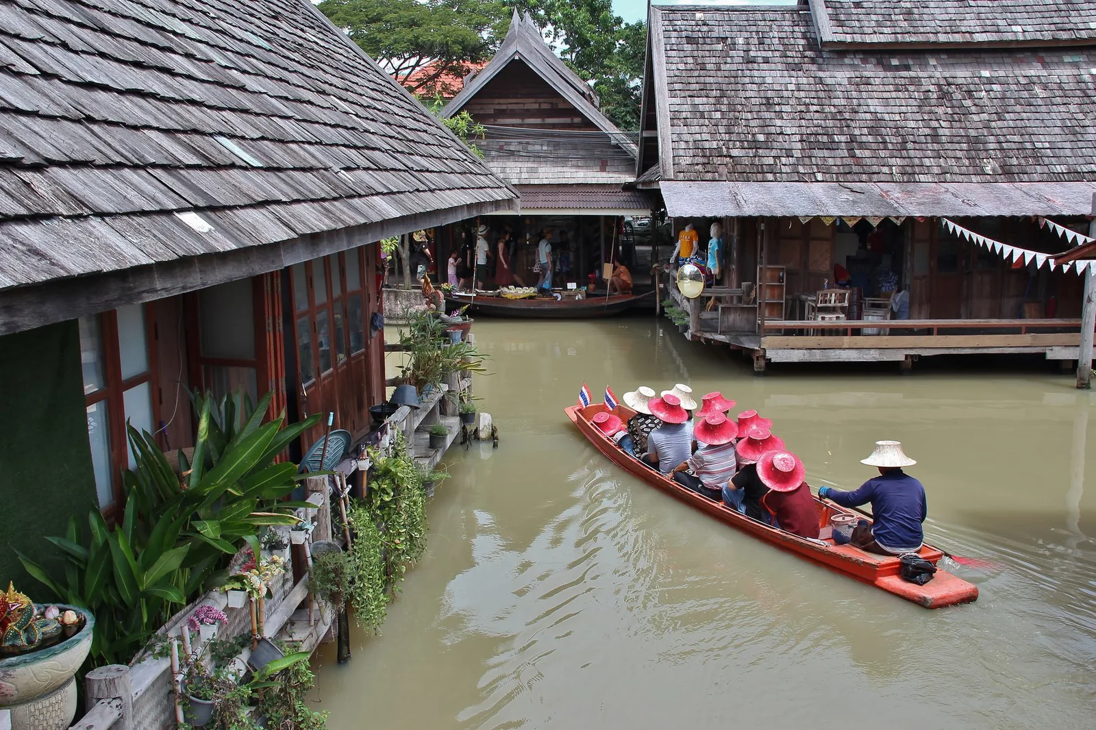 A long-tail boat cruising along a canal lined with traditional wooden houses of a Thai floating market