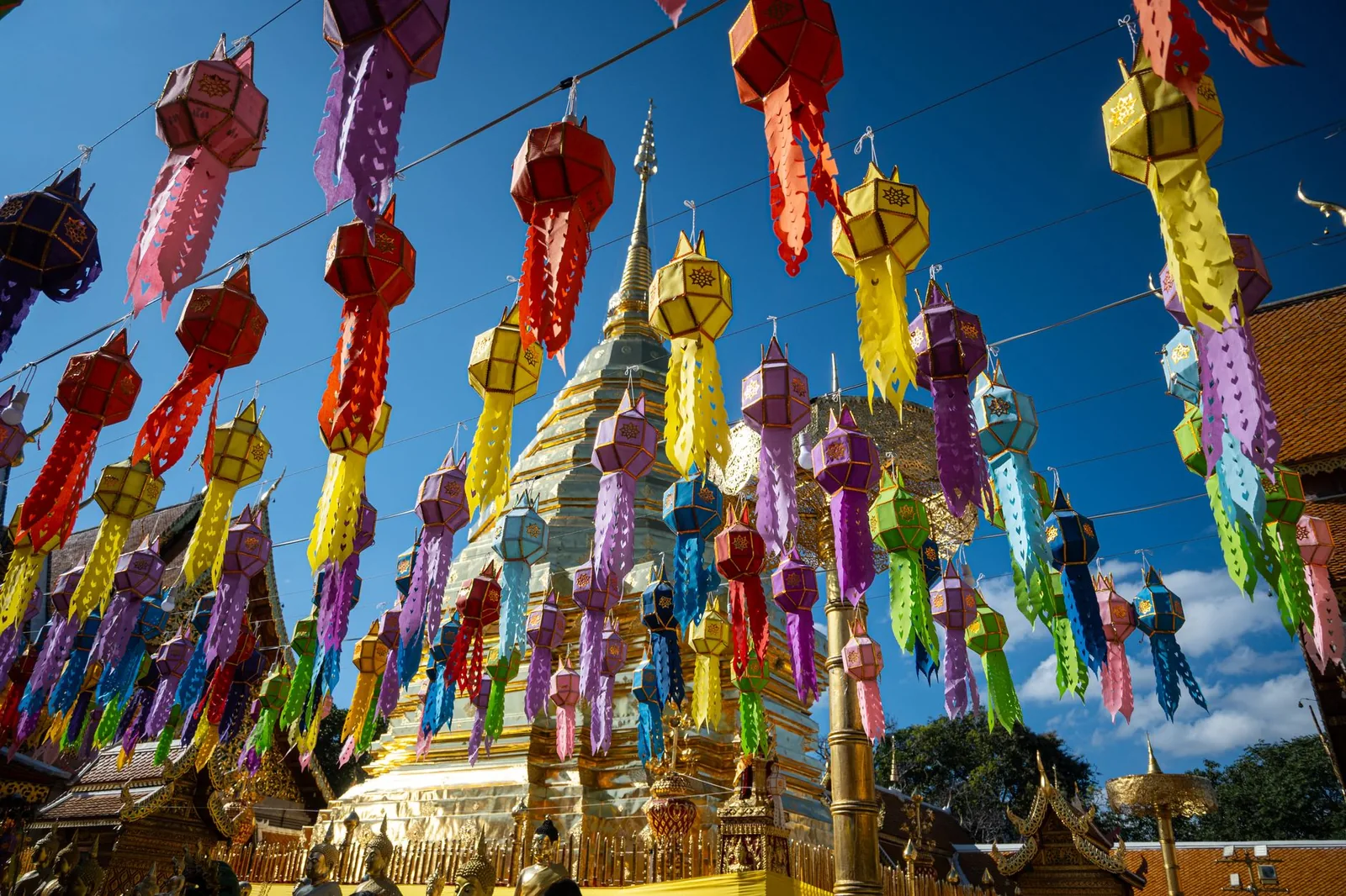 The Wat Phra That Doi Suthep temple in Chiang Mai, golden chedi adorned with colorful lanterns under a bright blue sky