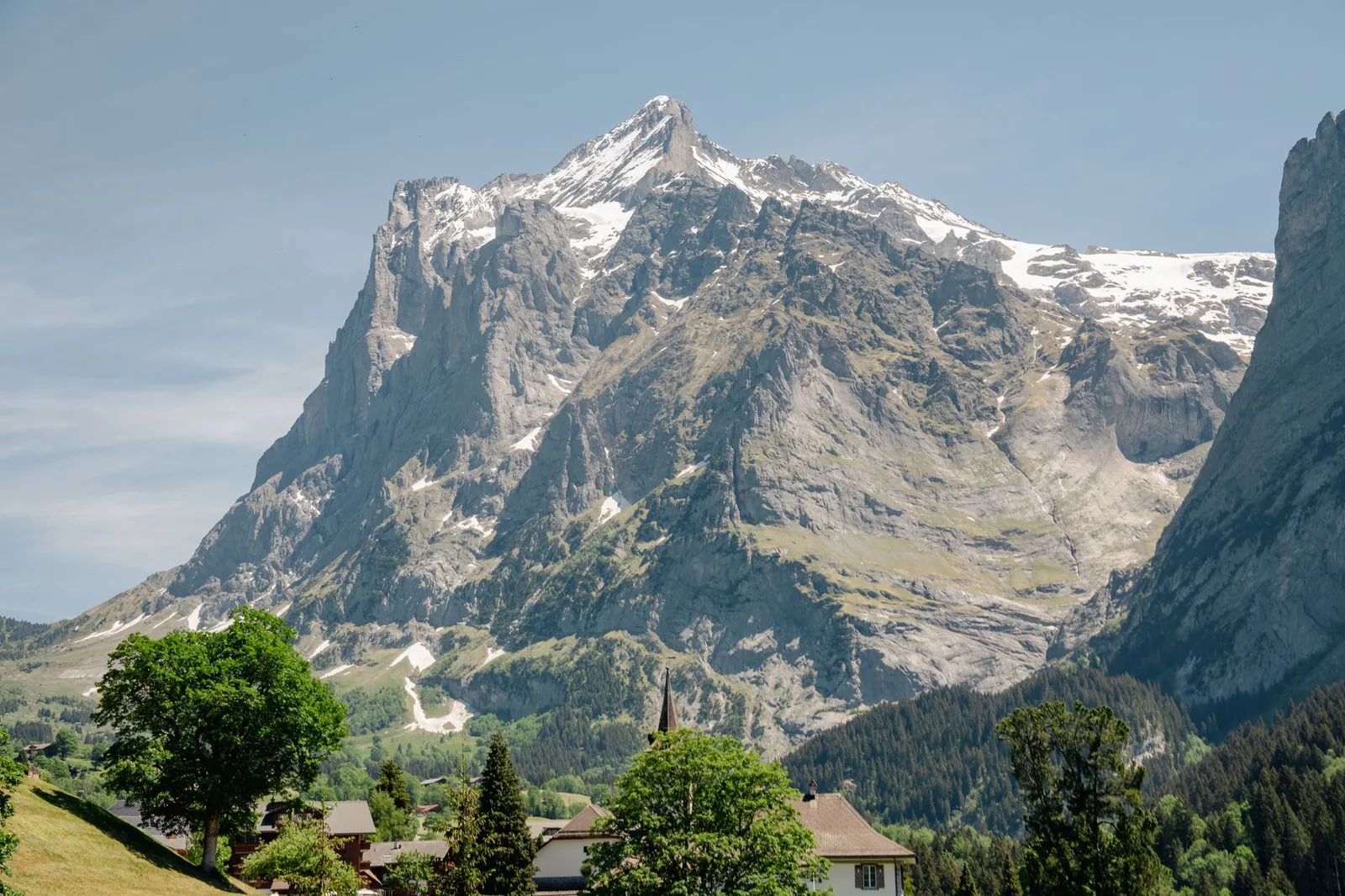 The sunlit alpine village of Grindelwald facing the Wetterhorn peak, green meadows and blue sky, Switzerland