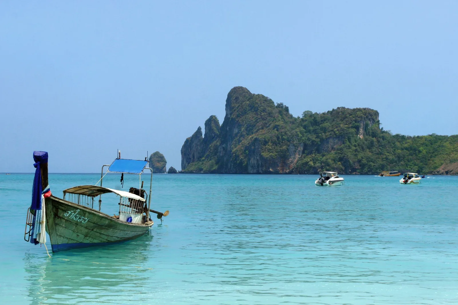 A wooden long-tail boat floating on turquoise waters near a Thai island on a sunny day