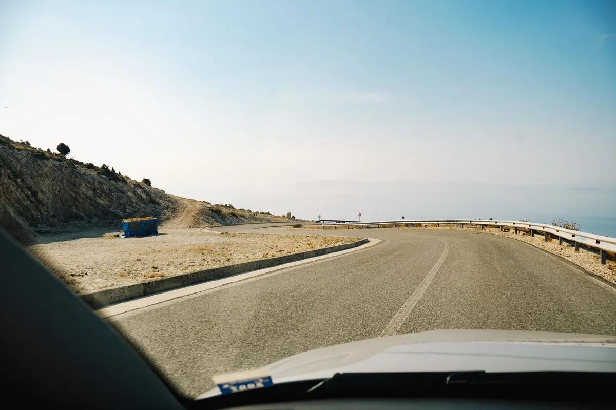 Winding Llogara pass road descending in switchbacks toward the turquoise Albanian Riviera coastline far below