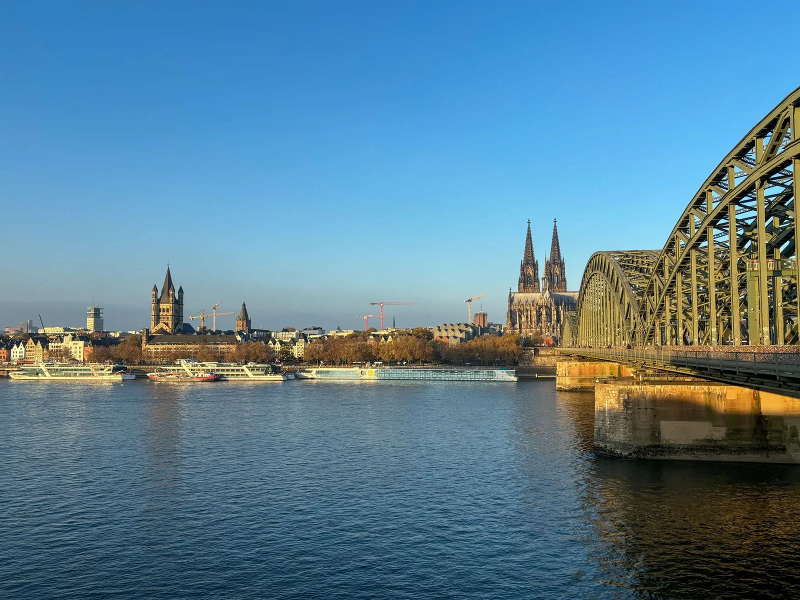 La catedral gótica de Colonia y el puente Hohenzollern reflejándose en el Rin bajo un cielo azul despejado