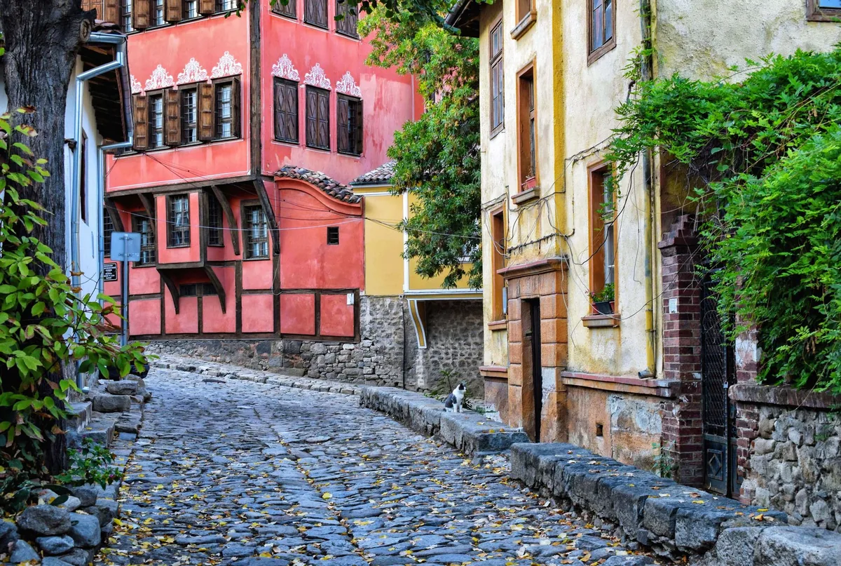 Calle empedrada del casco antiguo otomano de Gjirokastër, Albania, con casas de piedra y bazar, y un viajero consultando su teléfono