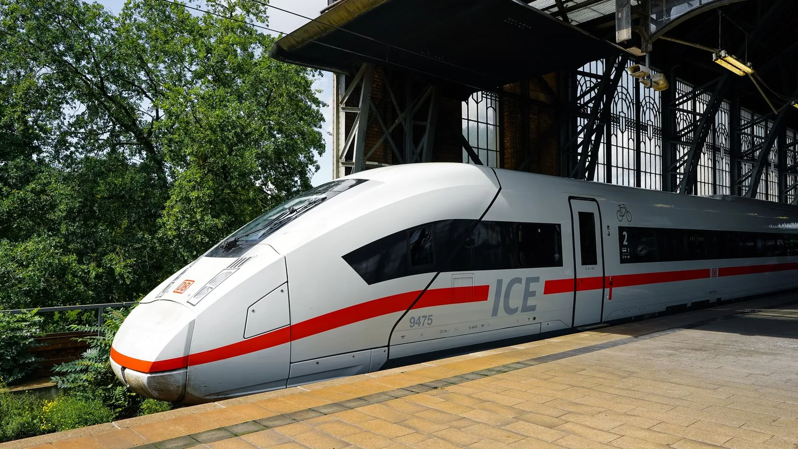 White ICE high-speed train beside a German station platform on a sunny day, its signature red stripe along the body