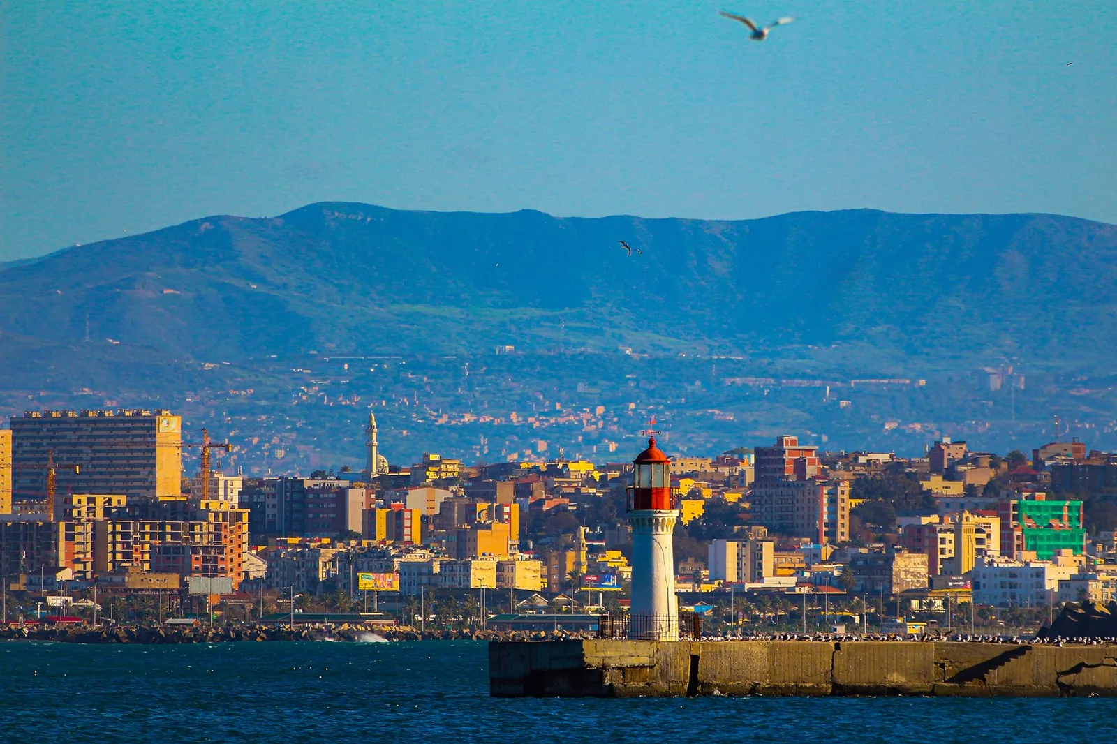 Front de mer d'Oran avec son phare, la ville et les montagnes sous un ciel bleu