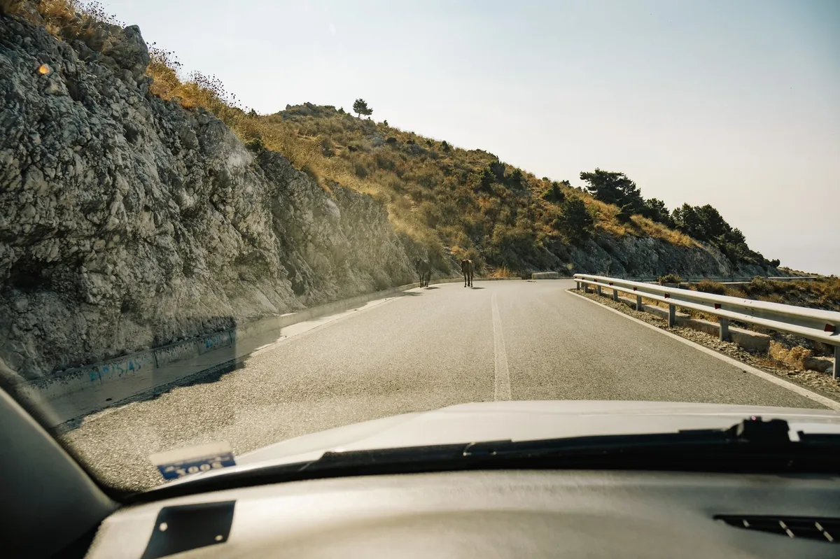 Coche en la carretera del puerto de Llogara en Albania, con vistas al mar Jónico y la Riviera albanesa al fondo y curvas cerradas en la bajada