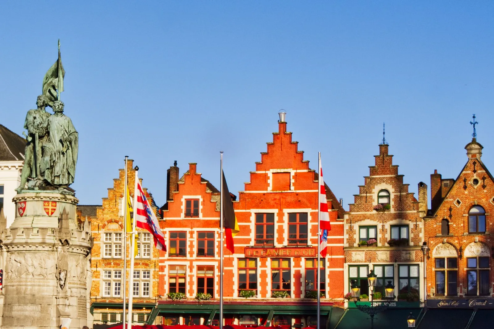 Maisons flamandes à pignons colorés bordant la place du Marché de Bruges sous un ciel bleu ensoleillé