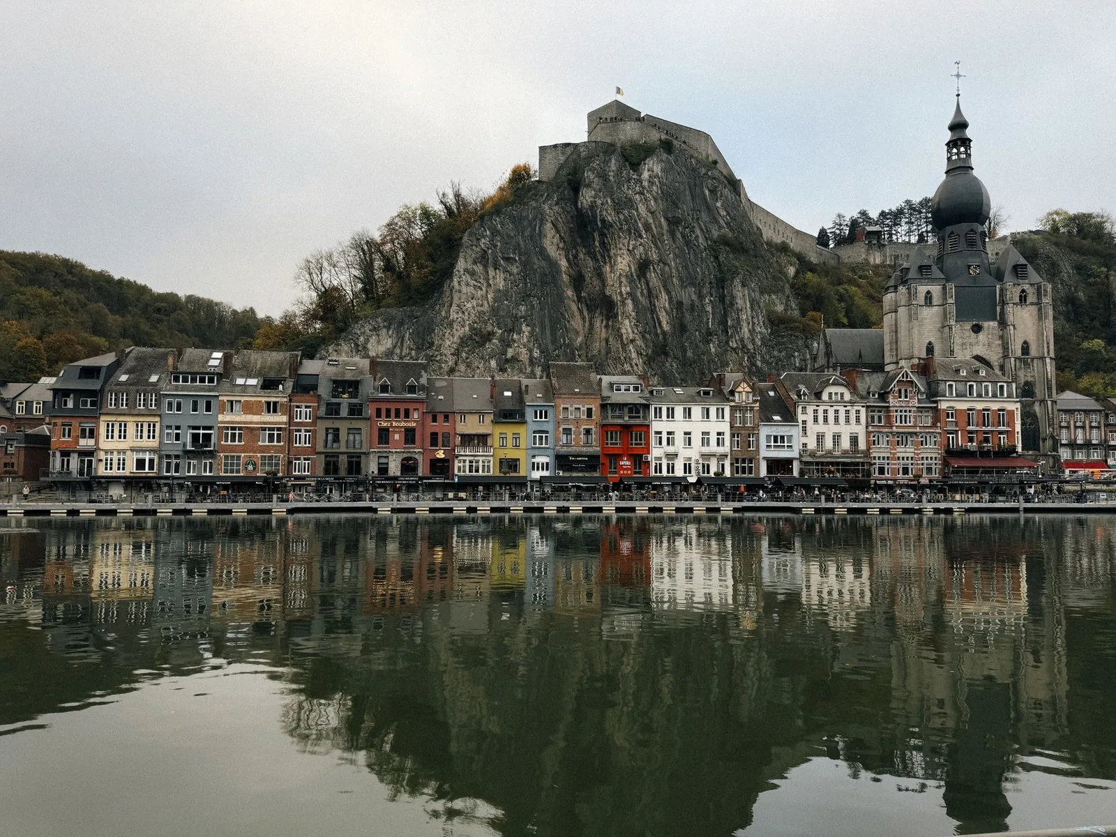 The colourful houses of Dinant along the Meuse river, below the citadel cliff and the bulbous bell tower of the collegiate church