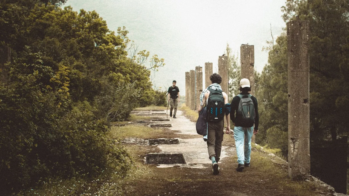 Pilgrims walking a country path through green Galicia towards Santiago de Compostela, walking poles and scallop shells on their backpacks, yellow waymarker stone