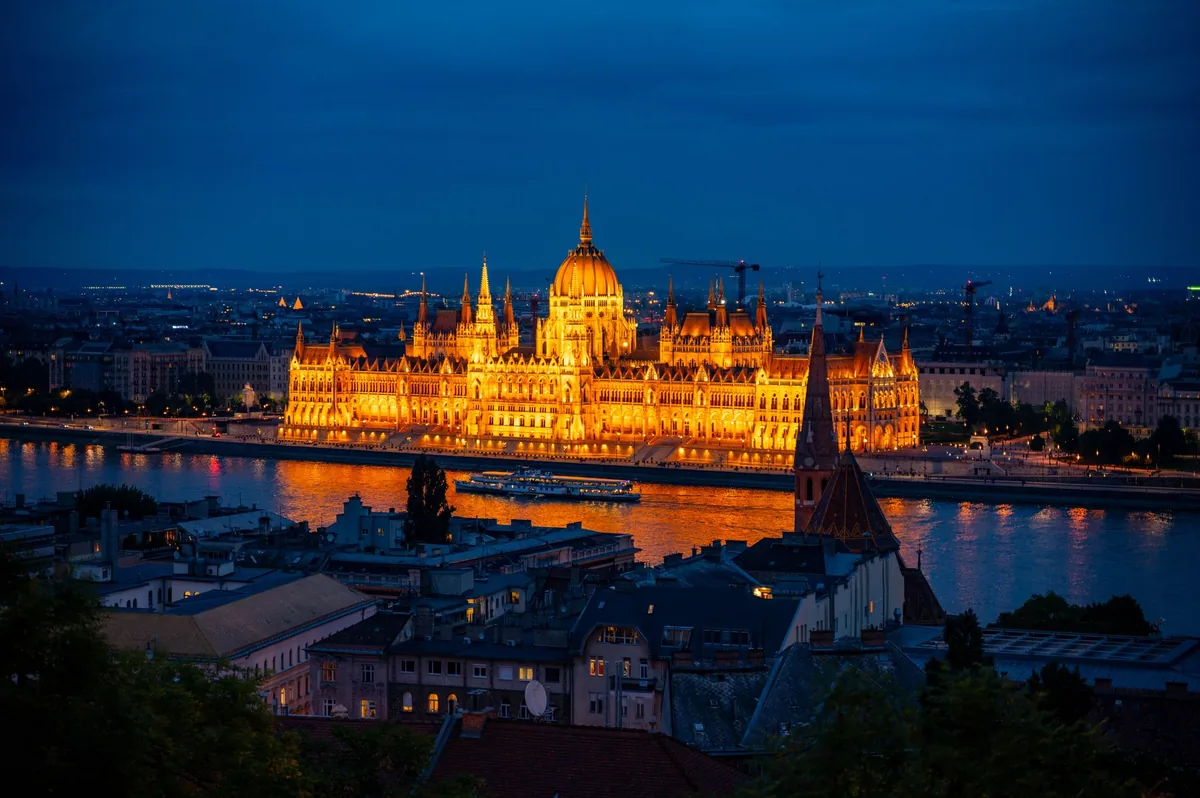 Vue sur le Parlement de Budapest illuminé au bord du Danube la nuit, avec le pont des Chaînes en arrière-plan