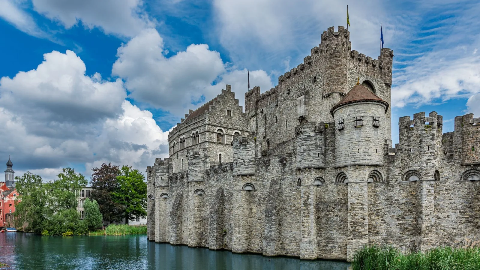 Le château des Comtes de Gand, forteresse médiévale en pierre et ses douves, sous un ciel bleu nuageux