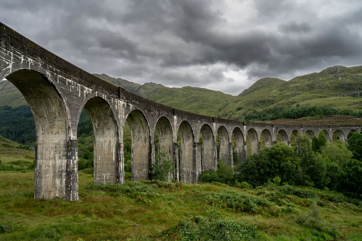 Regional train crossing a tall stone viaduct in the Swiss Alps, a green valley below and snow on the peaks