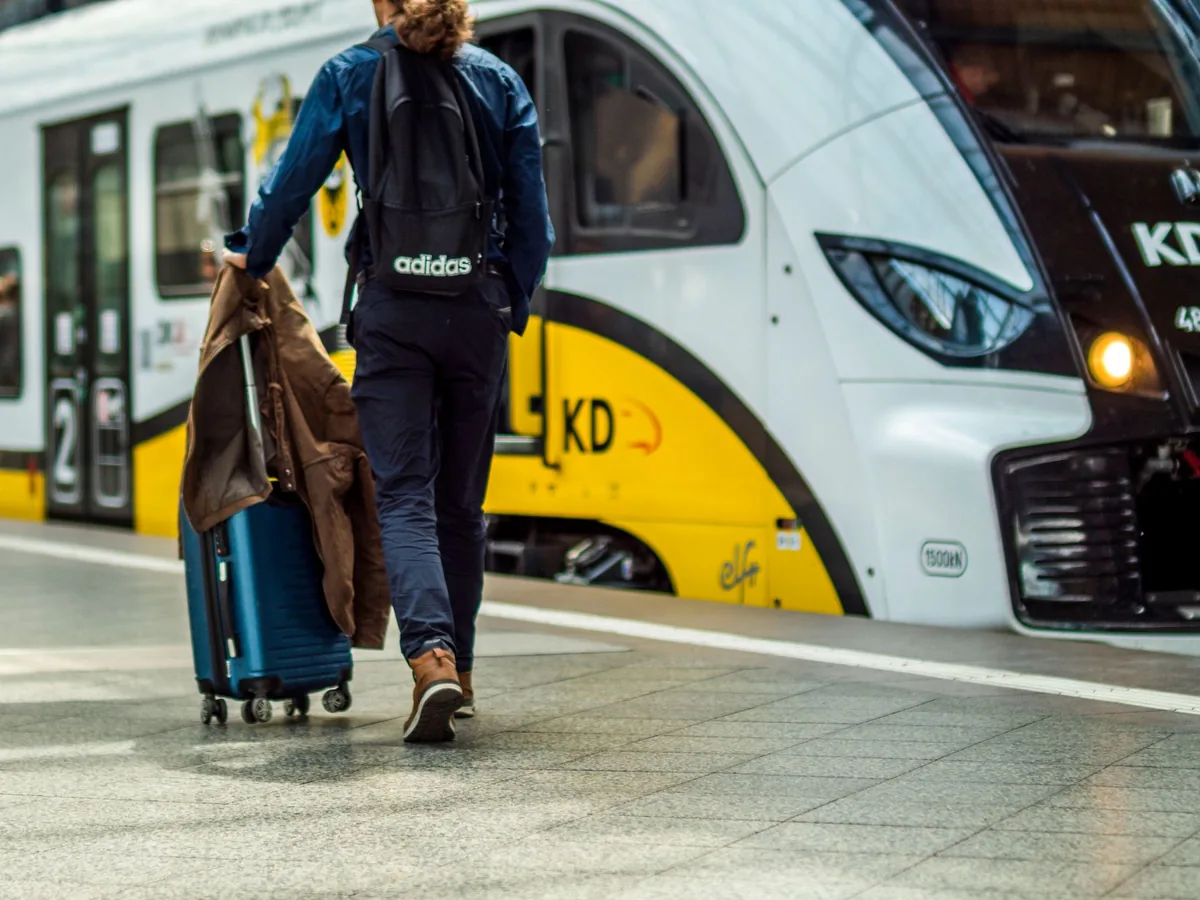 Voyageur sur un quai de gare européen consultant une application de billets de train sur son smartphone, train à quai