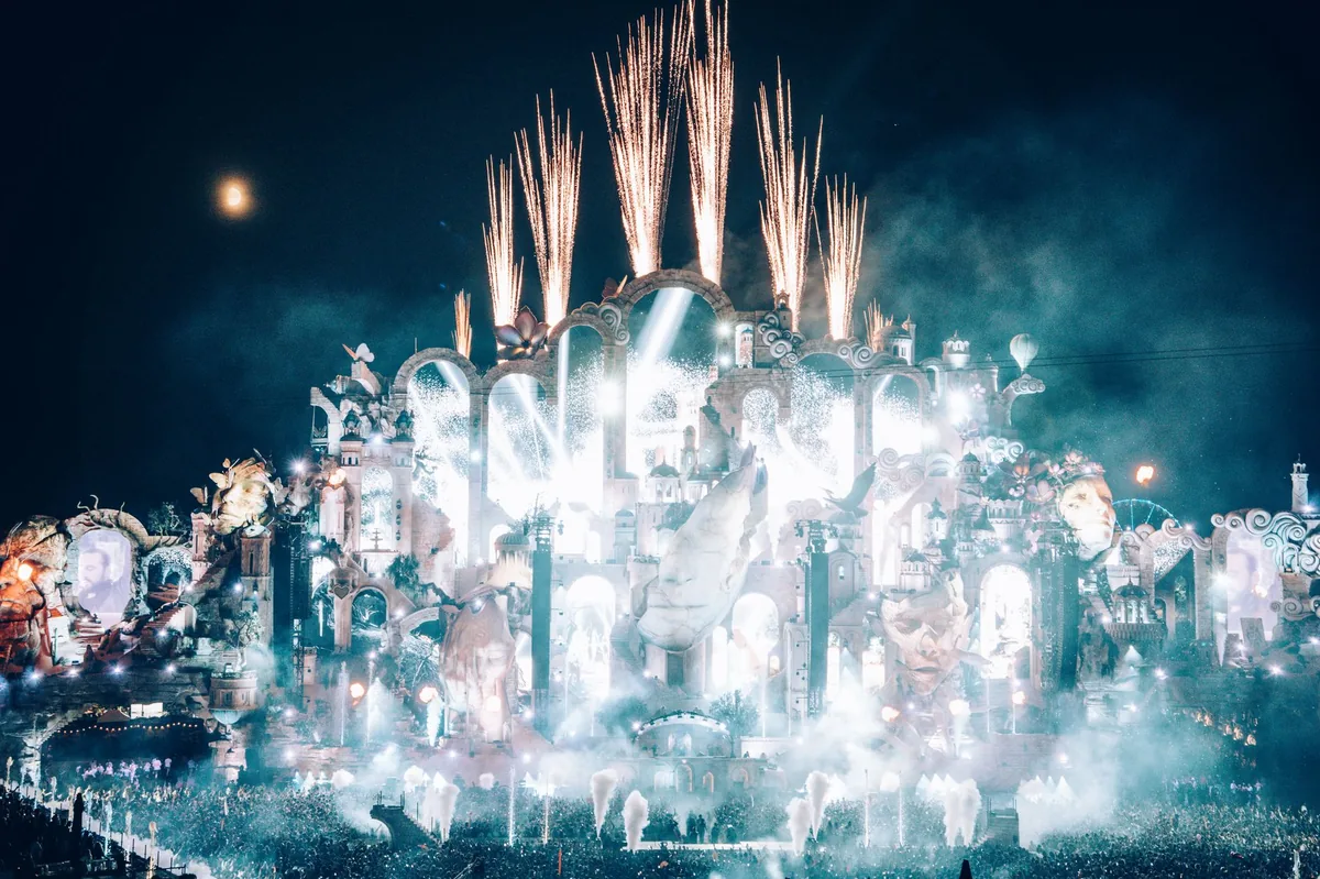 Foule devant la grande scène de Tomorrowland à Boom en Belgique au coucher du soleil, décor de scène monumental et jeux de lumière