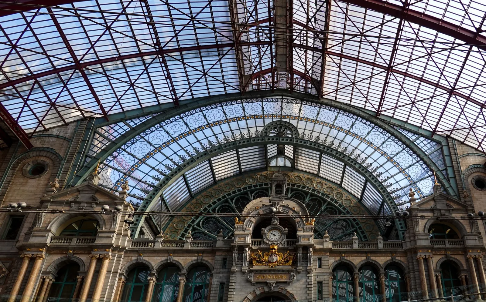 The monumental stone and steel vaulted roof of Antwerp Central station, with its gilded clock and richly ornamented dome