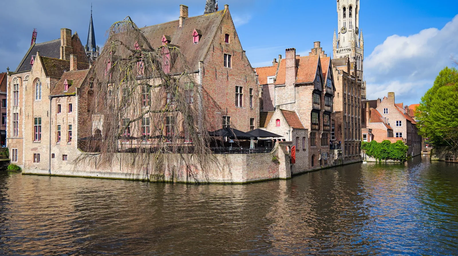 Canal de Brujas en el muelle del Rosario con los reflejos de las casas medievales de tejados a dos aguas y el campanario al fondo, bajo la luz dorada de la mañana