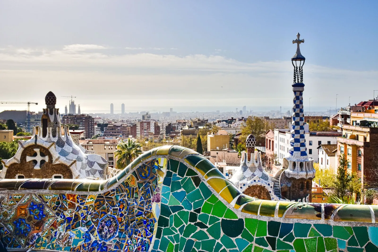 Colorful mosaics of Gaudí's Park Güell overlooking the rooftops of Barcelona down to the sea
