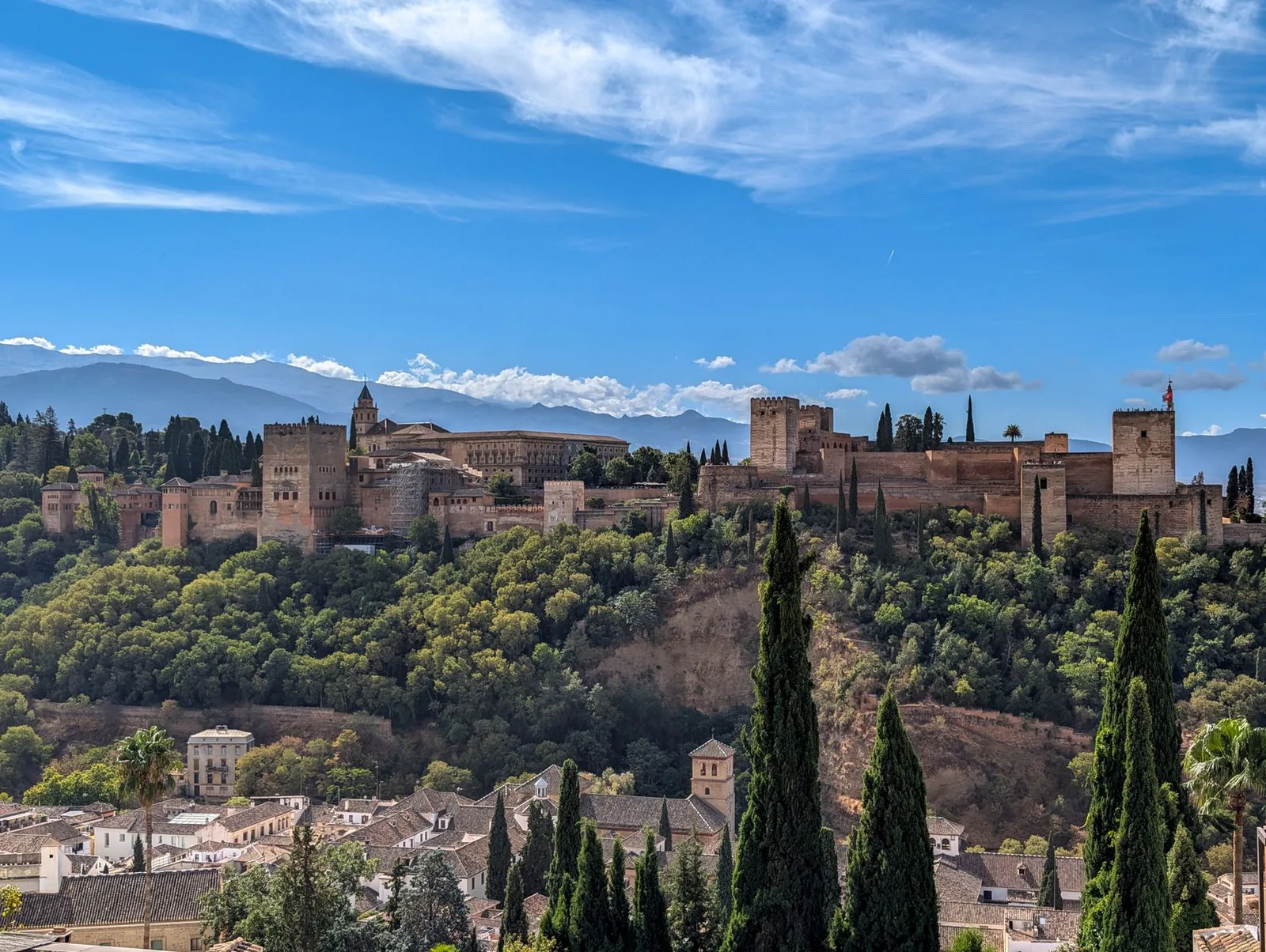 La Alhambra de Granada sobre su colina arbolada con Sierra Nevada nevada al fondo