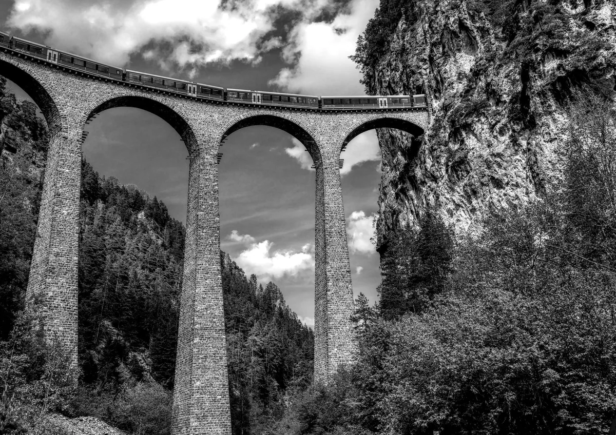 Tren regional cruzando un viaducto de piedra en los Alpes suizos, con un valle verde al fondo